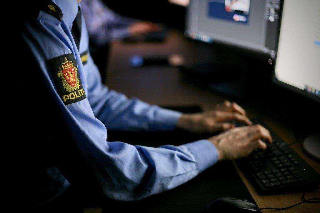 Bildet viser en person med politiuniform som sitter foran to skjermer og skriver på et tastatur