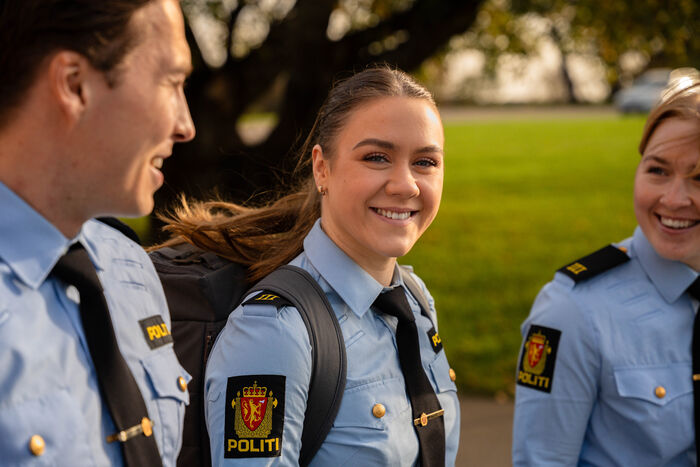 Tre politistudenter går ved siden av hverandre utendørs. De har blå uniform.