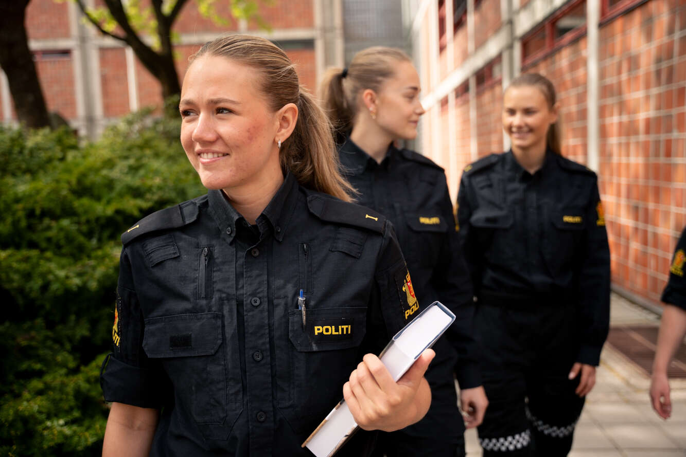 To smilende kvinnelige politistudenter går utendørs. En av dem bærer på flere bøker.