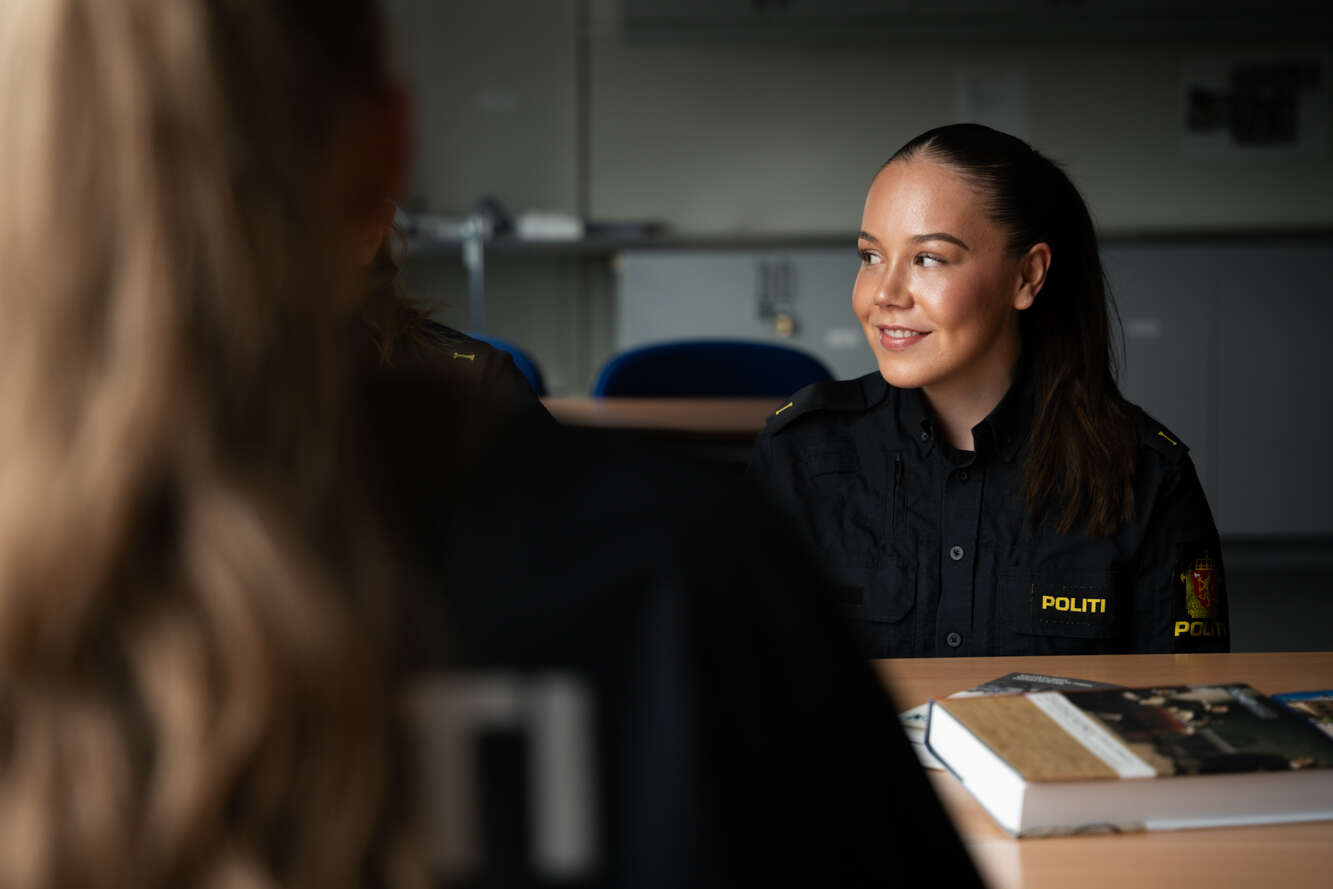 En jente i politiuniform sitter i et klasserom