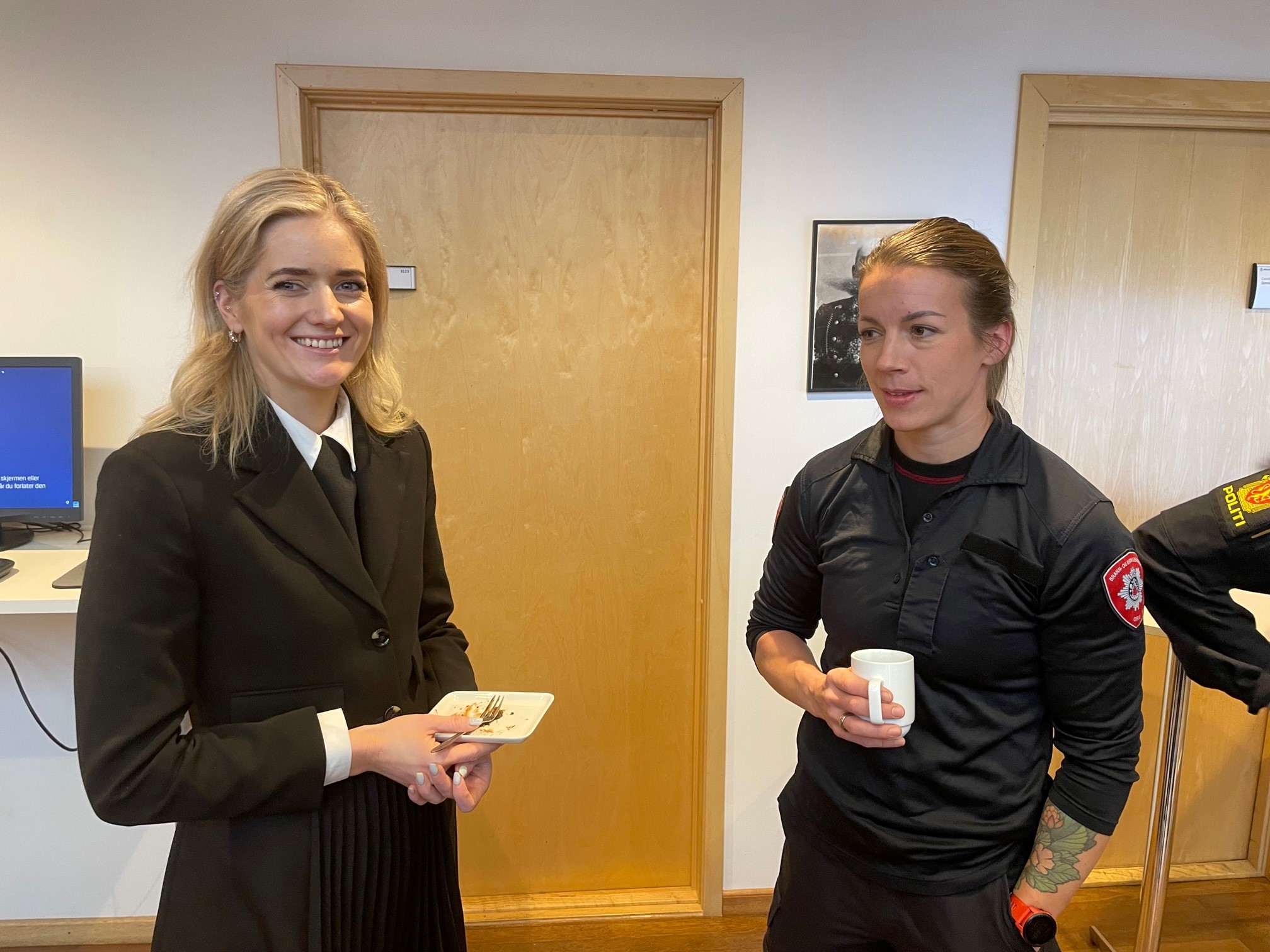 Bildet viser Emilie Enger Mehl, Norges justisminister, sammen med en ung kvinne i brannmann-uniform. Begge ser i kameraet og smiler.