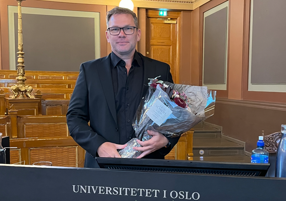 Knut M. Sørensen står med en bukett blomster og smiler til kamera. 