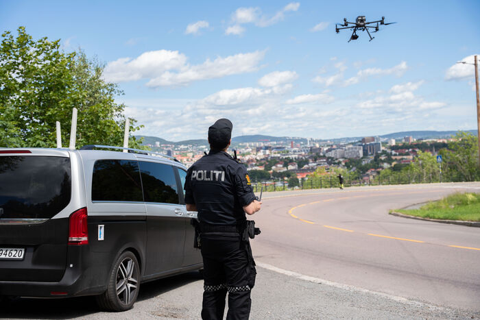 En politimann står med ryggen til kamera og flyr en drone. Det er også en varebil i bildet.