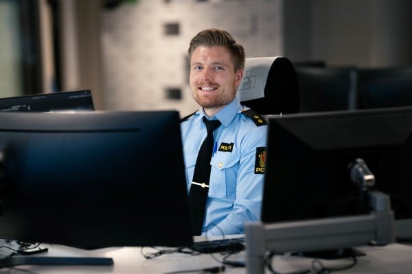 Operatør Anders sitter foran en PC-skjerm og smiler til kamera 