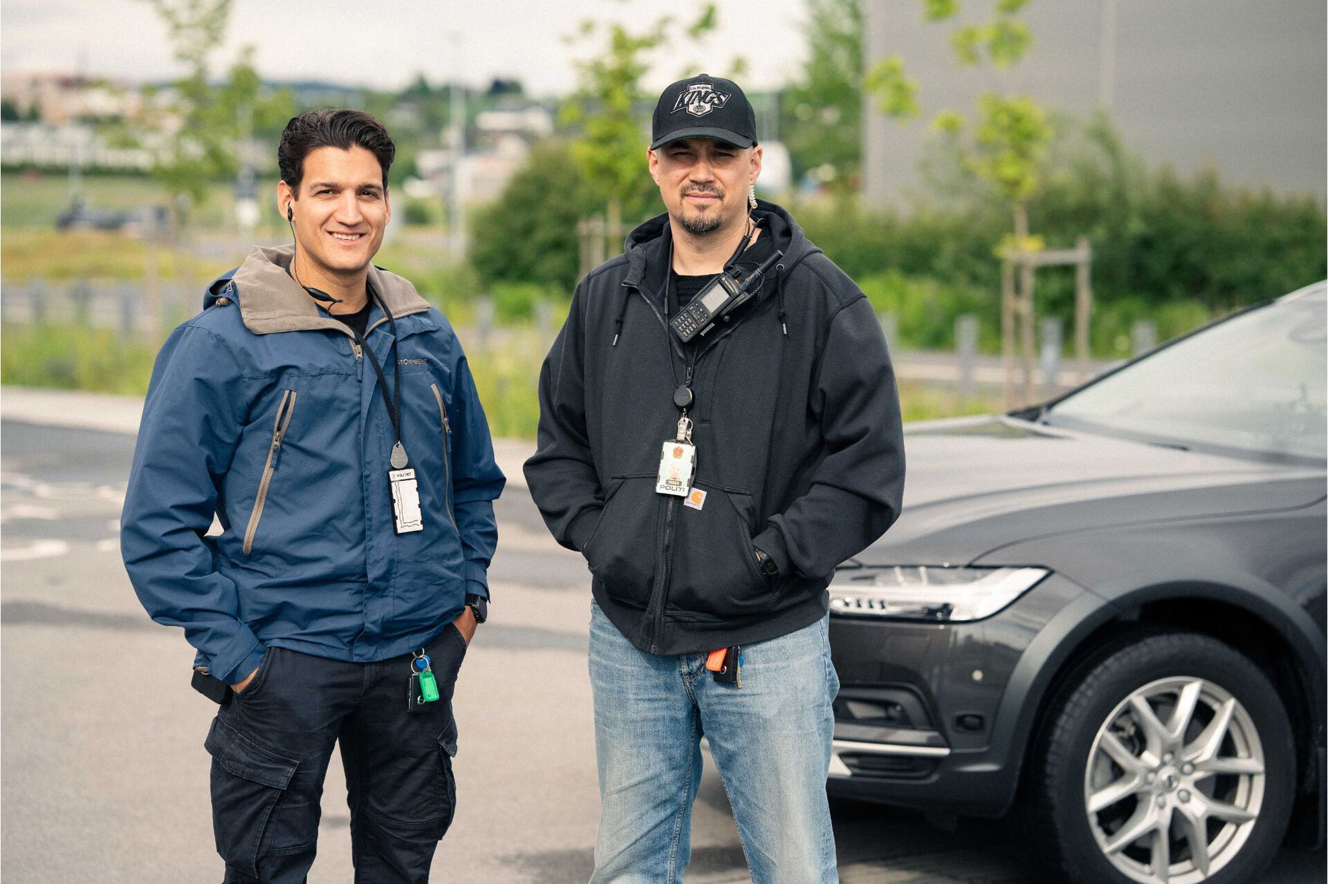 To politimenn kledd i sivilt står i helfigur og ser rett inn i kameraet.