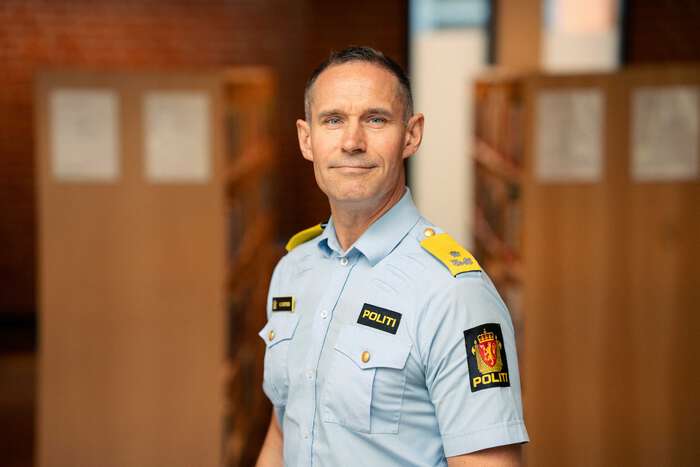 Mann i politiuniform foran bokhyller