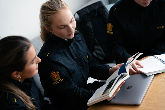 to jenter i politiuniform leser i en bok.