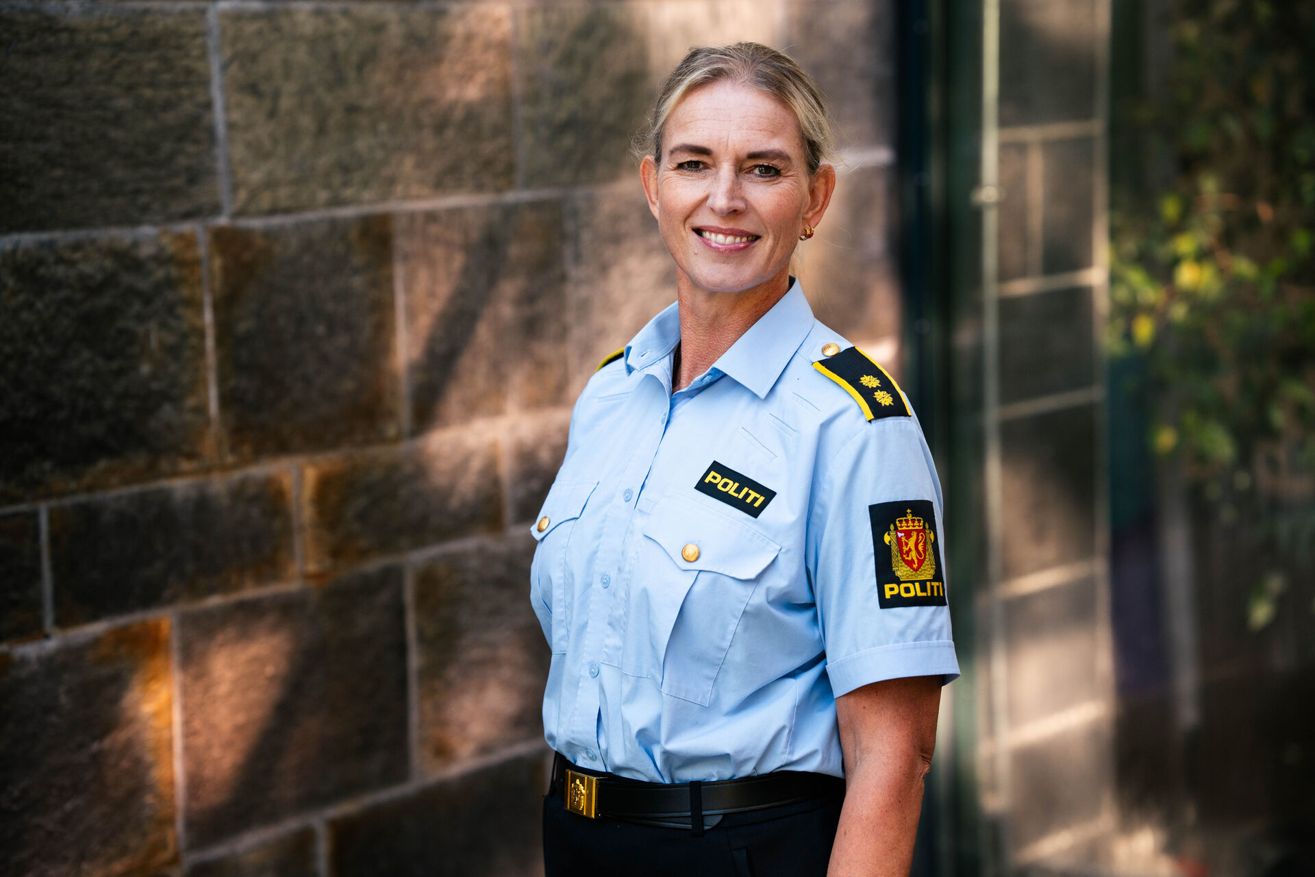 Wendy, en blond dame med politiuniform. Hun står foran en murvegg og smiler.