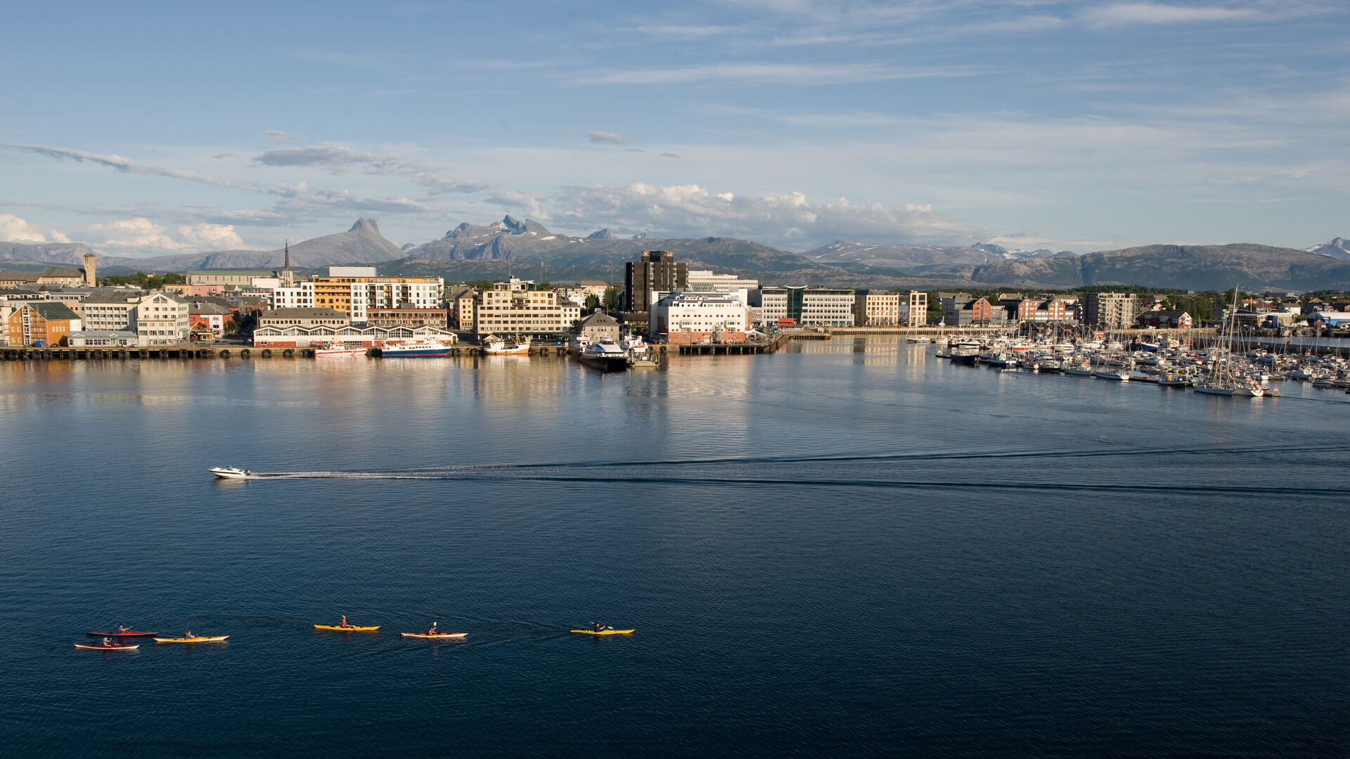 Oversiktbilde av Bodø by med havet foran. Tkajakkpadlere og en båt er på vei over vannet. 