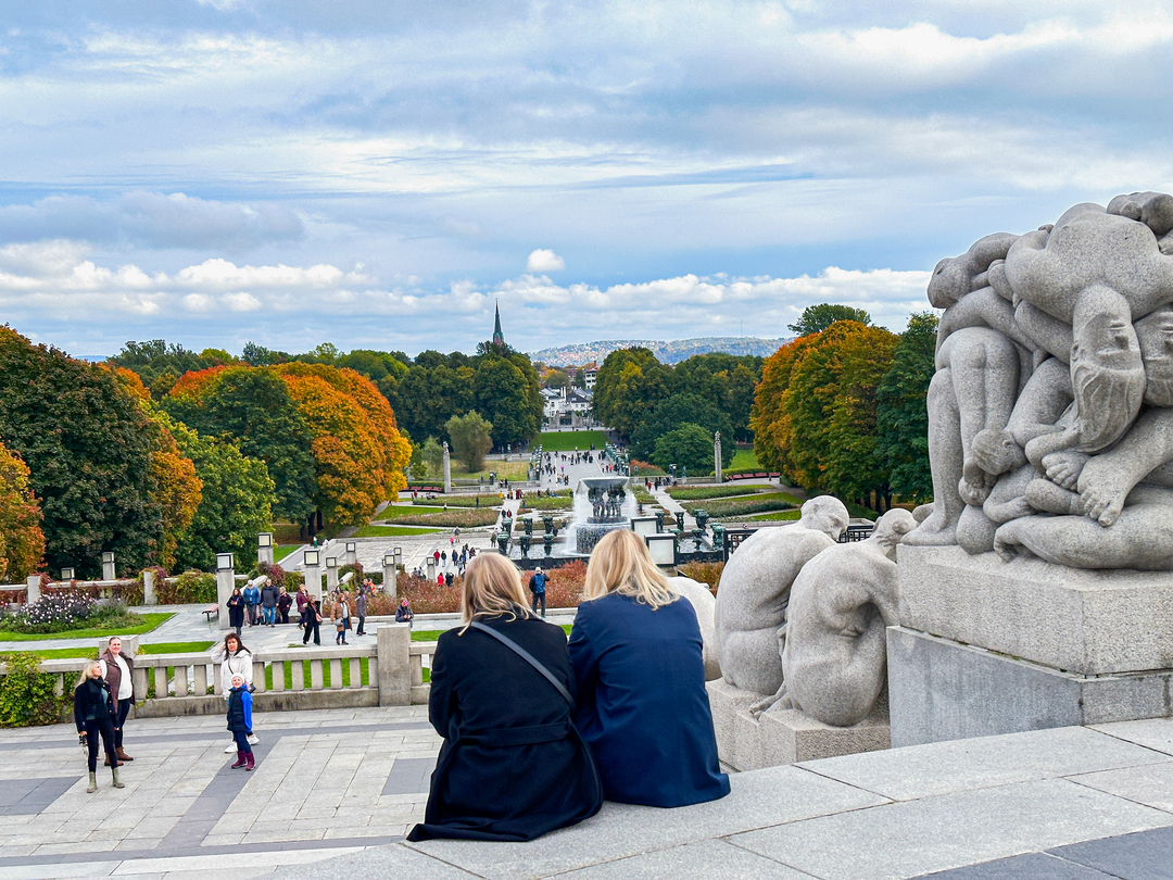 To jenter sitter i en trapp ved et par skulpturer og ser utover Frognerparken.