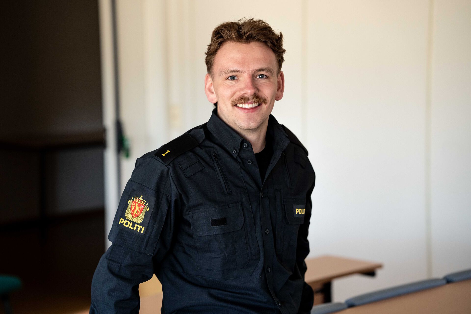 Politistudent Andreas smiler til kamera iført politiuniform