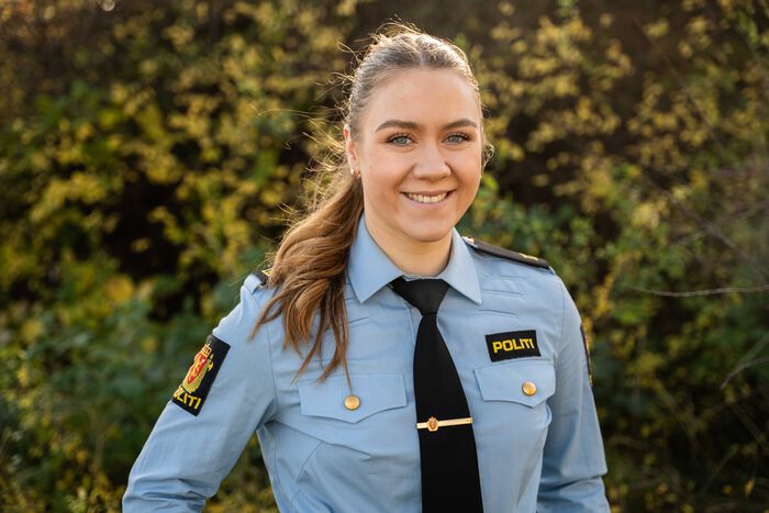 Ung kvinne med hestehale og politiuniform smiler inn i kamera.