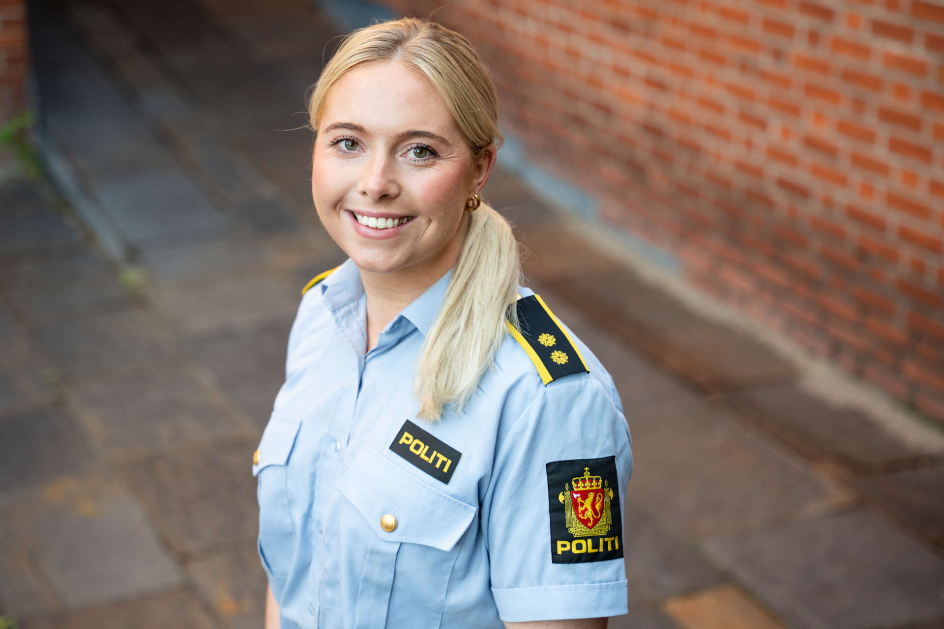Kvinne med blondt hår og politiuniform smiler til kamera