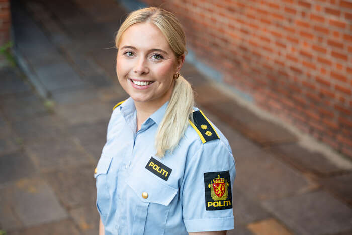 Kvinne med blondt hår og politiuniform smiler til kamera