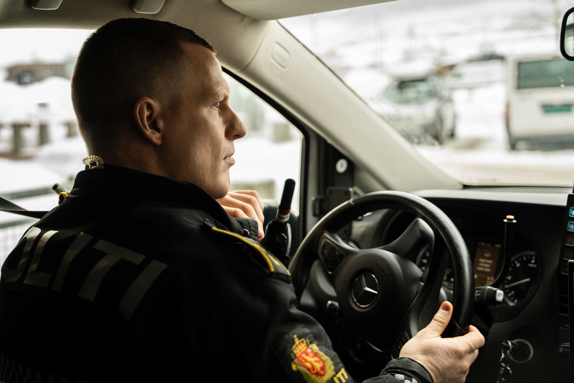 Bilde av politimann med kort hår bak rattet på en politibil.