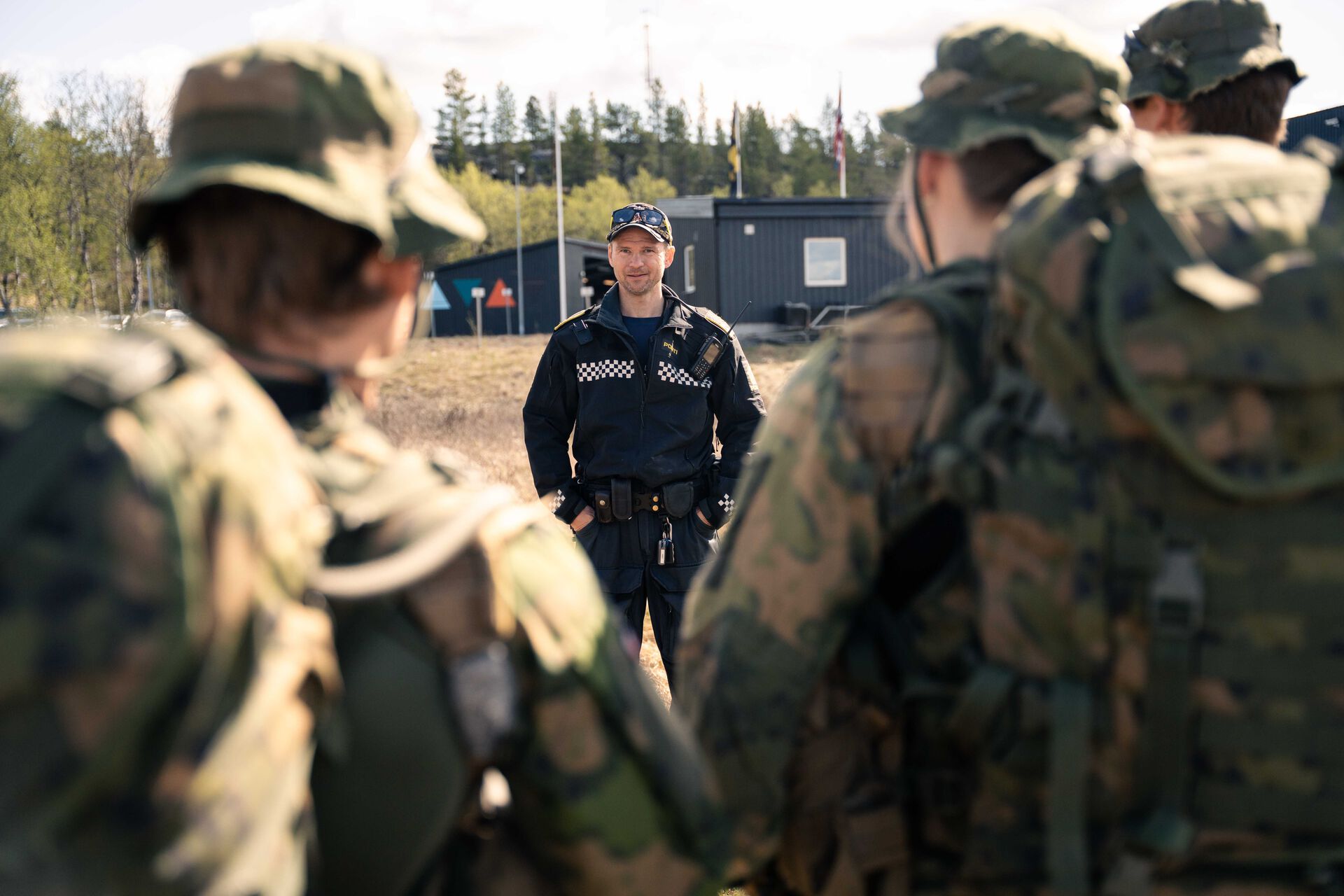 Mange soldater i uniform står med ryggen til kamera og ser på en politimann