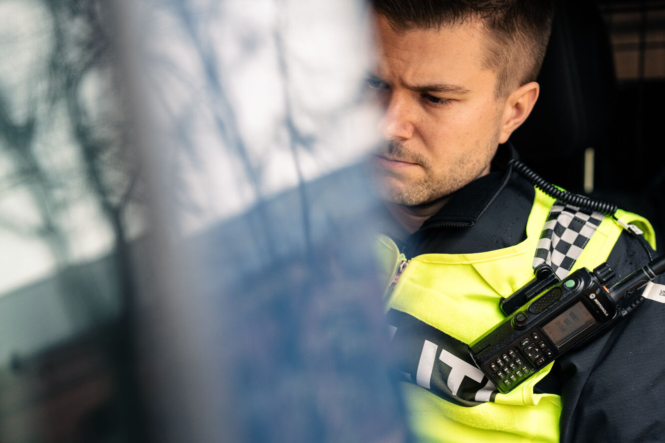 Politimann med vest og walkie talkie i bil
