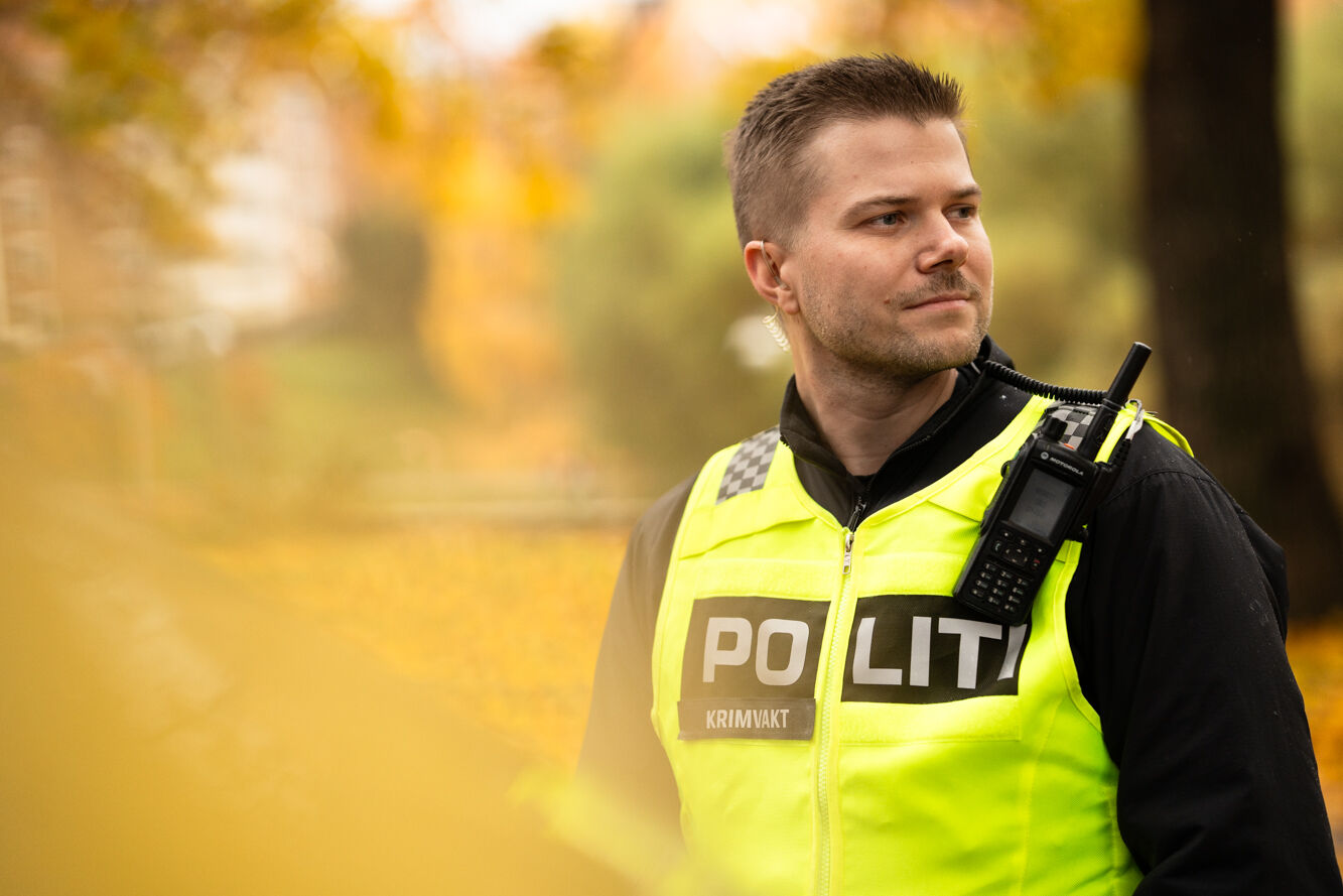 Politimann med kort hår i uniform med gul vest og walkie talkie