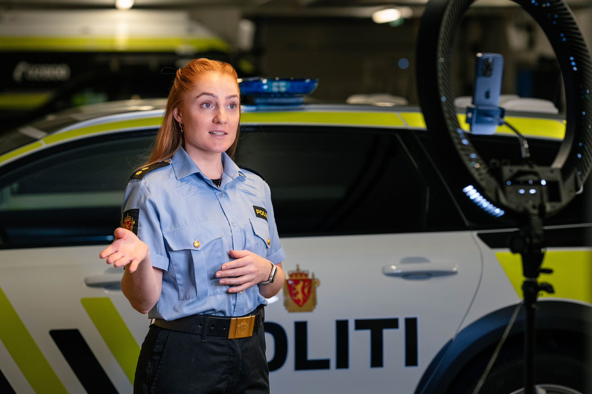 Gabriella is recording a movie on her phone. The phone is on a stative and she has a police car behind her. 